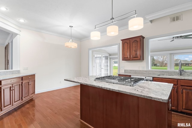 kitchen with dark wood-style flooring, stainless steel gas cooktop, visible vents, ornamental molding, and a sink