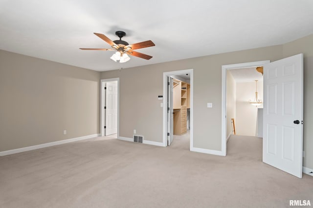 unfurnished bedroom featuring light carpet, baseboards, visible vents, ceiling fan, and a walk in closet