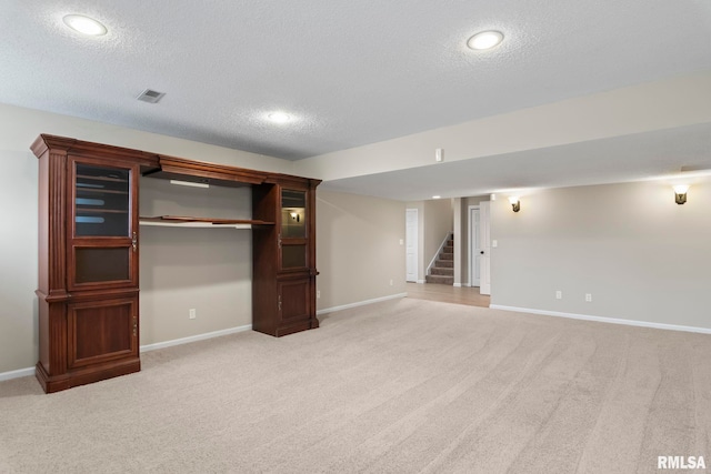 finished basement with light carpet, stairway, a textured ceiling, and baseboards