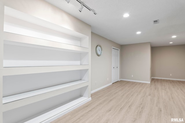 empty room featuring light wood finished floors, built in shelves, baseboards, and recessed lighting