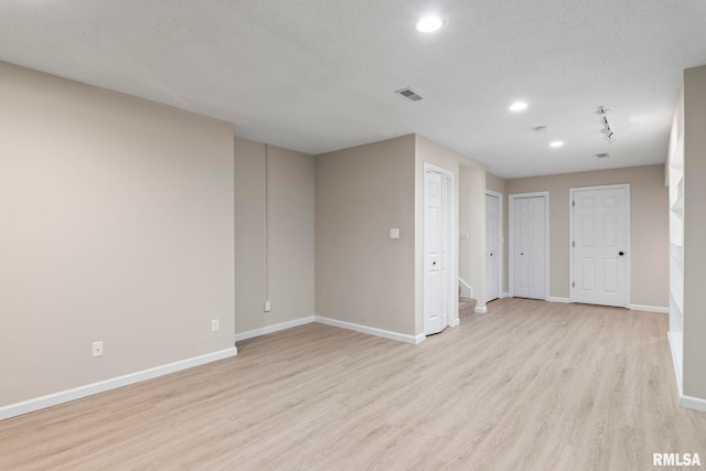 empty room featuring baseboards, light wood-style flooring, visible vents, and a textured ceiling