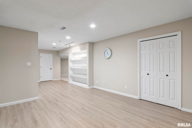 interior space with a textured ceiling, light wood-style floors, visible vents, and baseboards