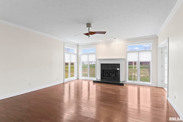 unfurnished living room featuring a healthy amount of sunlight, ornamental molding, wood finished floors, and a high end fireplace