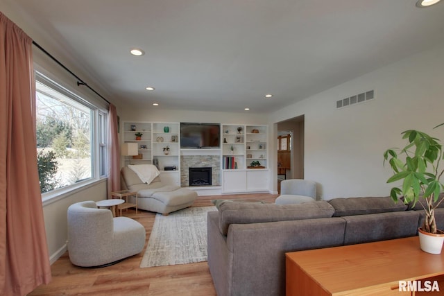 living area featuring visible vents, baseboards, a stone fireplace, light wood-style floors, and recessed lighting