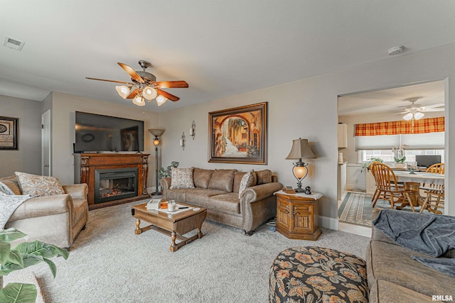 living room with ceiling fan, light colored carpet, visible vents, baseboards, and a glass covered fireplace