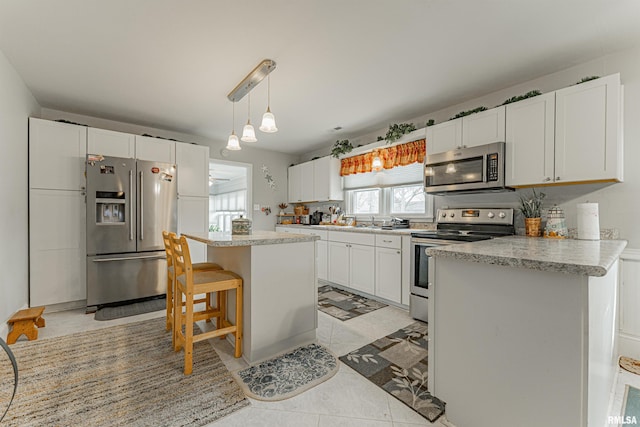 kitchen featuring a kitchen island, appliances with stainless steel finishes, hanging light fixtures, light countertops, and white cabinetry