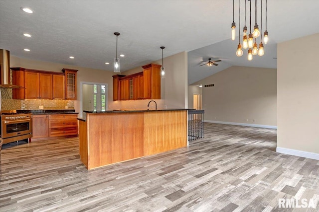 kitchen with stainless steel range with gas stovetop, open floor plan, light wood finished floors, and brown cabinets