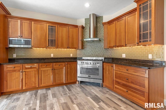 kitchen featuring brown cabinets, light wood finished floors, wall chimney exhaust hood, stainless steel appliances, and backsplash