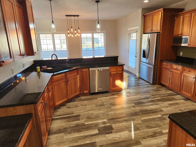 kitchen with stainless steel appliances, brown cabinetry, a sink, and dark wood-style flooring