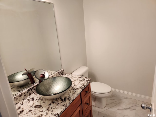 bathroom with toilet, baseboards, marble finish floor, and vanity