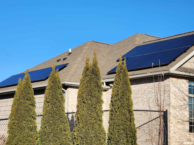 view of side of property featuring roof mounted solar panels, fence, roof with shingles, and brick siding