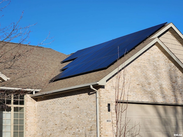 view of home's exterior with roof mounted solar panels, a shingled roof, and brick siding