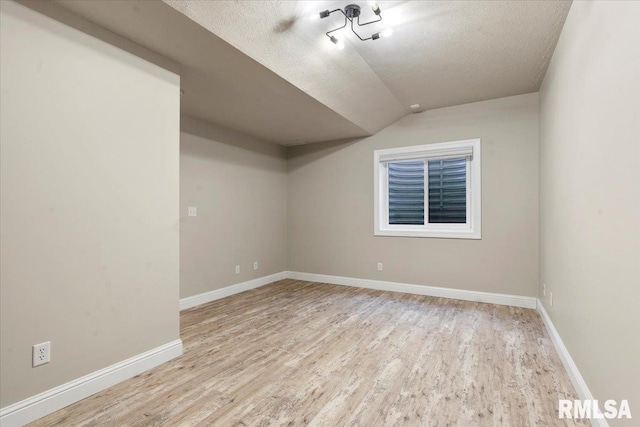 unfurnished room featuring baseboards, a textured ceiling, lofted ceiling, and wood finished floors