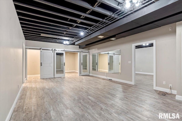 below grade area with baseboards, a barn door, and wood finished floors