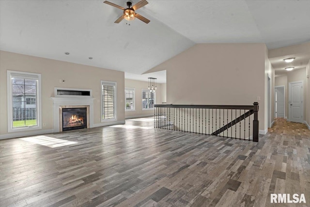 unfurnished living room featuring lofted ceiling, a healthy amount of sunlight, wood finished floors, and ceiling fan with notable chandelier
