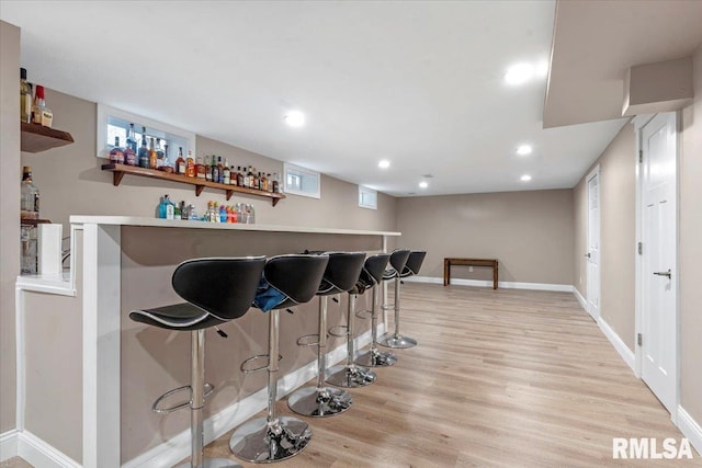 bar featuring light wood-type flooring, baseboards, a bar, and recessed lighting