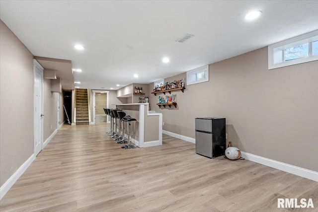 interior space featuring baseboards, a bar, freestanding refrigerator, and light wood-style floors