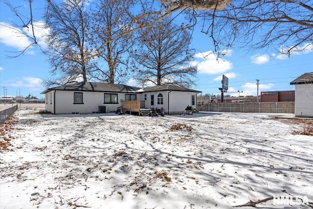 snow covered back of property featuring central AC, fence, and a wooden deck