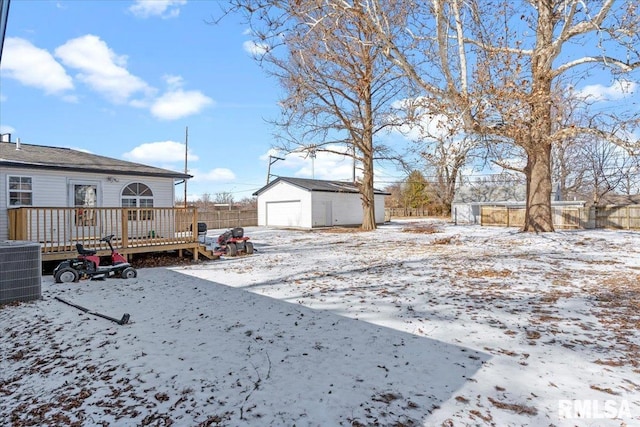 yard layered in snow featuring a garage, central AC unit, an outdoor structure, and a wooden deck