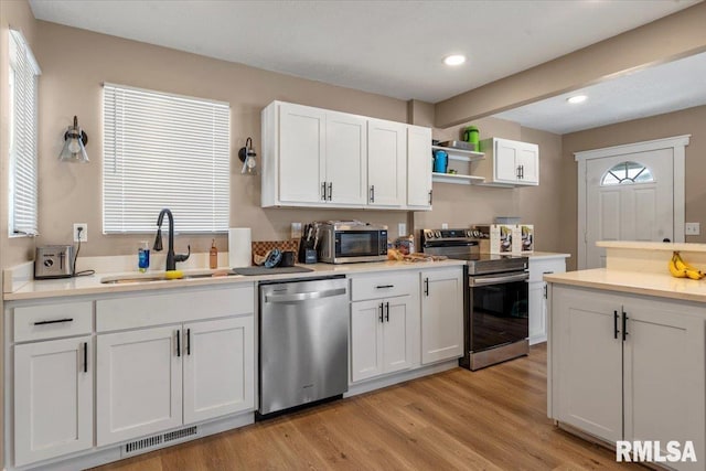 kitchen with stainless steel appliances, a sink, visible vents, white cabinets, and light countertops