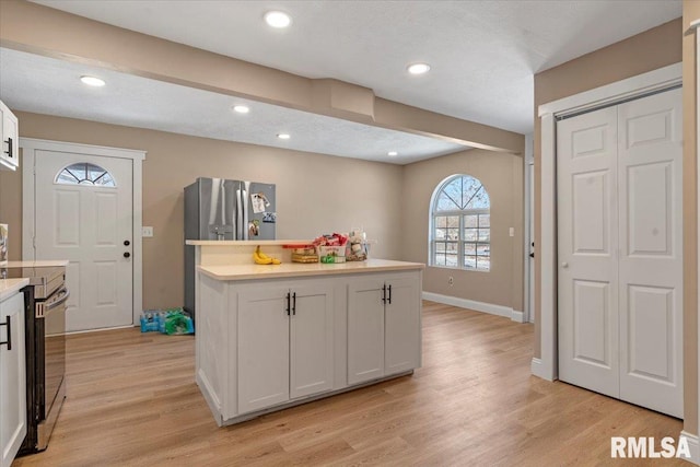 kitchen featuring stainless steel appliances, light wood-style floors, white cabinets, light countertops, and a center island