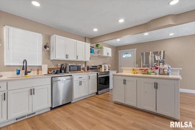 kitchen with white cabinets, light wood-style flooring, stainless steel appliances, light countertops, and a sink