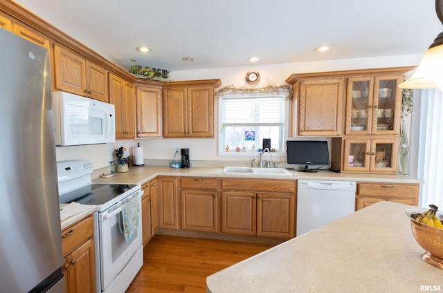 kitchen with white appliances, glass insert cabinets, light countertops, light wood-style floors, and a sink