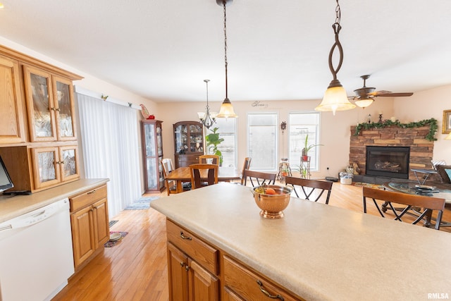 kitchen featuring light countertops, hanging light fixtures, light wood-style flooring, glass insert cabinets, and white dishwasher