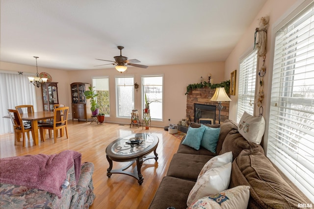 living area with ceiling fan with notable chandelier, a stone fireplace, and light wood-style flooring