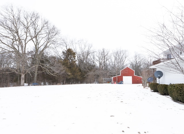 snowy yard featuring a detached garage, a barn, and an outdoor structure