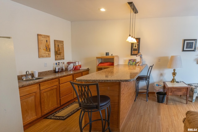 kitchen featuring light wood-style floors, a breakfast bar area, pendant lighting, and a sink