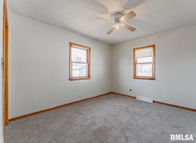 empty room with carpet floors, a healthy amount of sunlight, visible vents, and baseboards