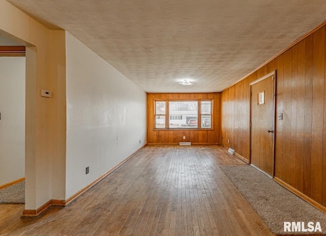 empty room featuring wooden walls, wood-type flooring, a textured ceiling, and baseboards