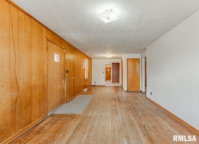 unfurnished room featuring light wood finished floors, baseboards, and wood walls