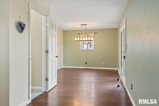 unfurnished dining area featuring dark wood-style flooring, an inviting chandelier, and baseboards