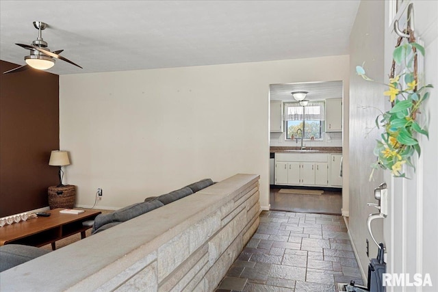 bathroom featuring baseboards, a sink, a ceiling fan, and stone tile floors