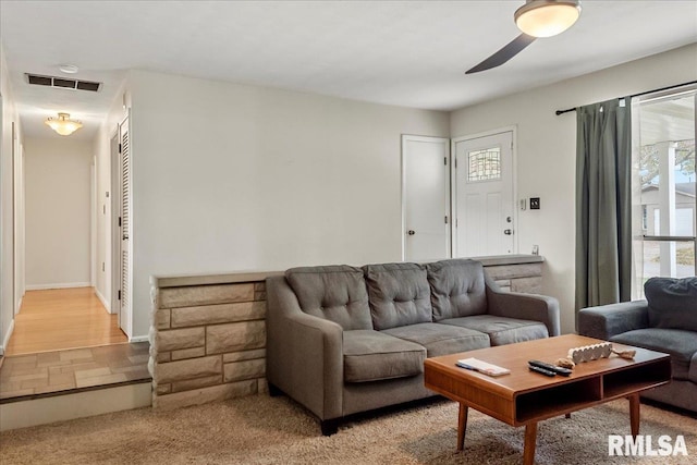 living room with baseboards, visible vents, a ceiling fan, and light colored carpet