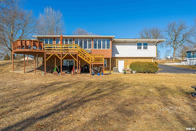 rear view of property featuring a sunroom, stone siding, a lawn, and a wooden deck