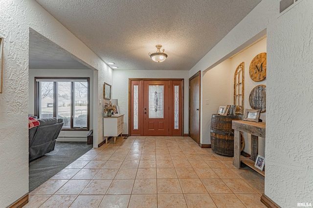 entrance foyer featuring visible vents, light tile patterned flooring, a textured ceiling, and a textured wall