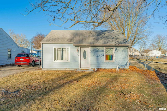 view of front facade featuring driveway, a shingled roof, fence, and a front yard