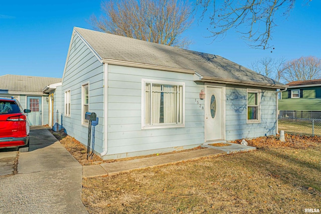 bungalow-style house with driveway, fence, a front lawn, and roof with shingles