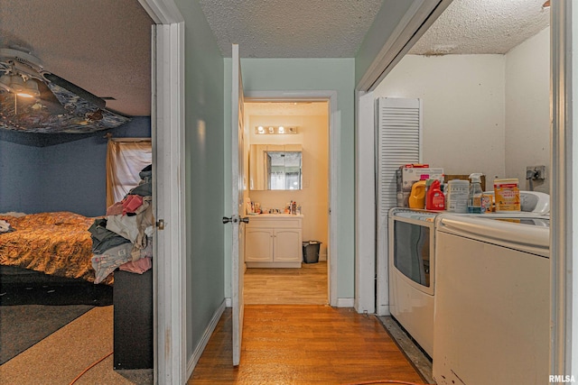 corridor featuring a textured ceiling, washer and clothes dryer, light wood-style flooring, and baseboards