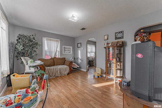 living room with arched walkways, baseboards, visible vents, and light wood-style floors