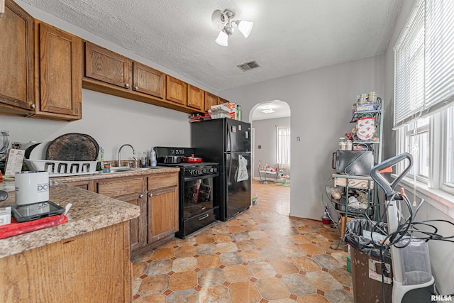 kitchen featuring arched walkways, black appliances, visible vents, and brown cabinets