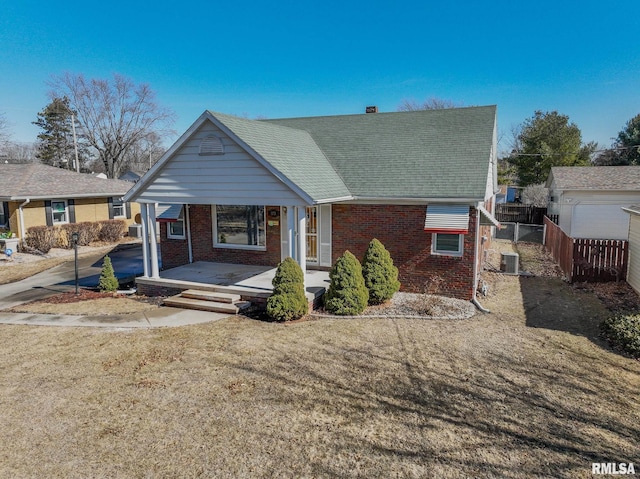 bungalow-style house with fence, central air condition unit, a front lawn, a porch, and brick siding