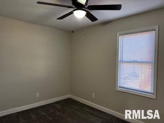 spare room featuring baseboards, dark carpet, and ceiling fan