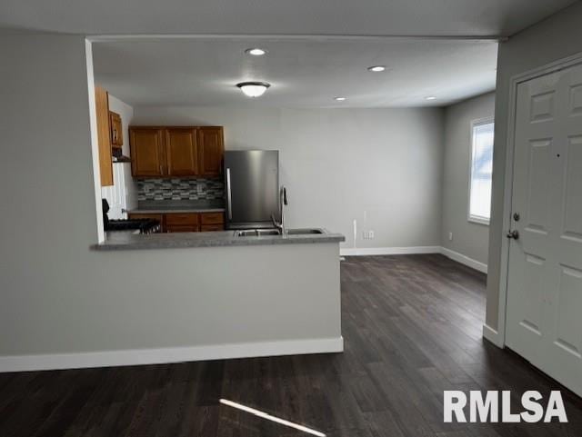 kitchen with dark wood-style flooring, tasteful backsplash, brown cabinetry, freestanding refrigerator, and a sink