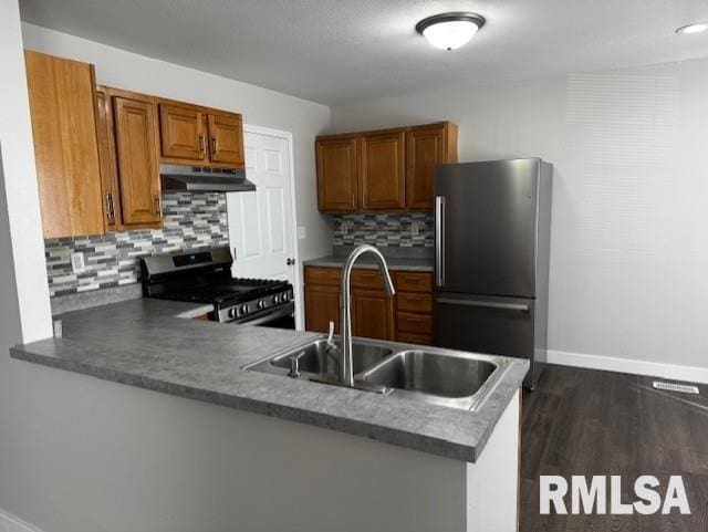 kitchen featuring brown cabinets, appliances with stainless steel finishes, a sink, a peninsula, and under cabinet range hood