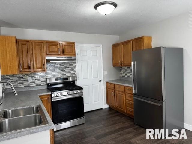 kitchen featuring under cabinet range hood, stainless steel appliances, a sink, brown cabinets, and dark wood-style floors