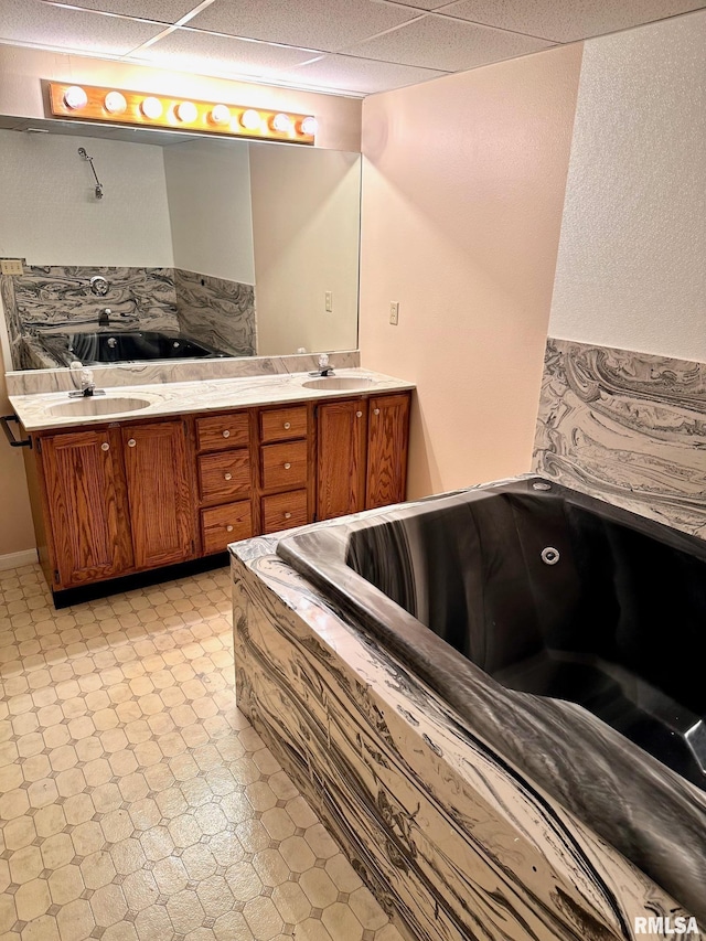 bathroom with a paneled ceiling, tile patterned floors, a sink, and double vanity